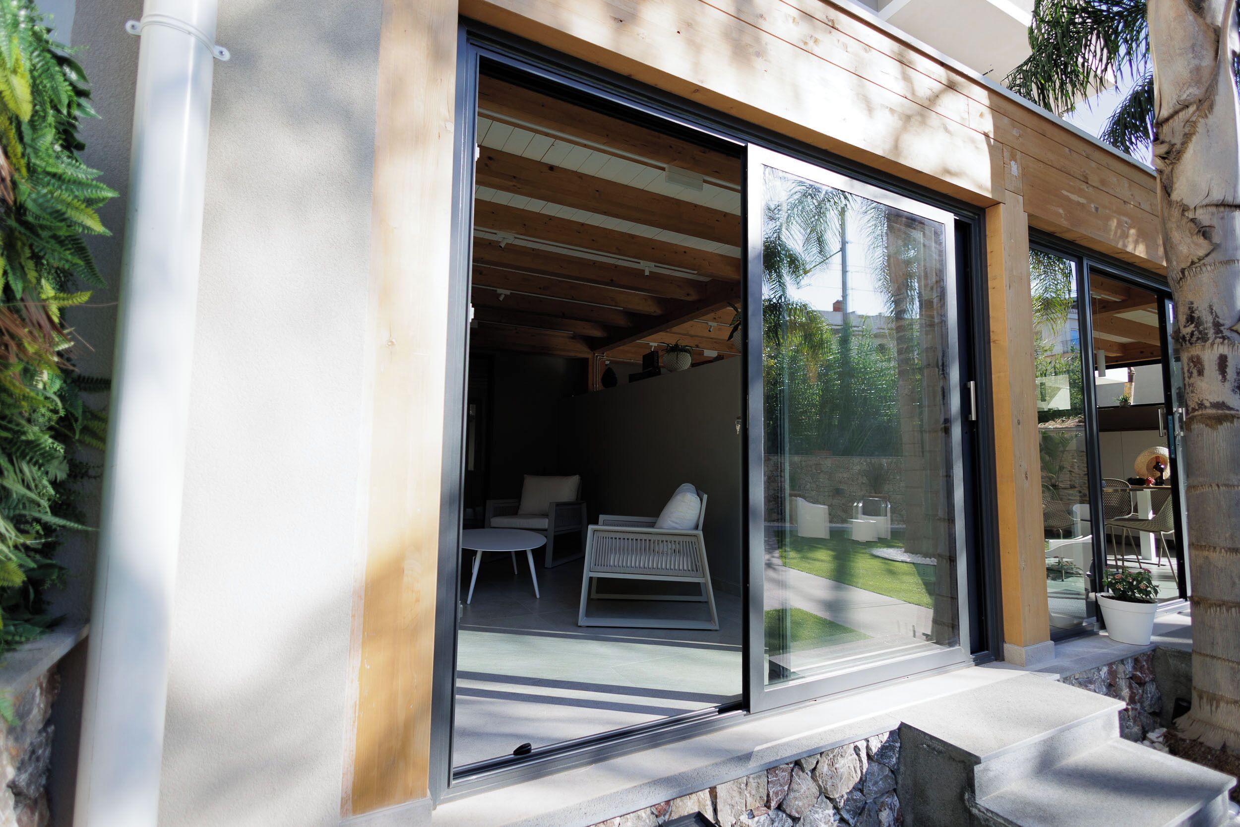 A modern building with large sliding glass doors leading to an outdoor seating area with a table and chairs.