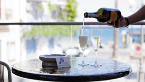 A bottle of champagne being poured into two glasses on a round table with a nameplate. - SEA GARDEN LUXURY ROOMS (Giardini Naxos)