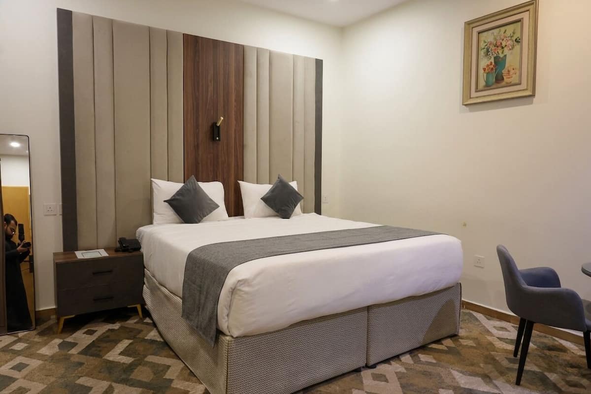 Una habitación de hotel con una cama grande, una mesita de noche, una silla y un cuadro en la pared.