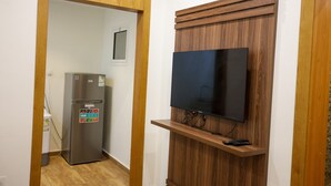 A compact room with a built-in TV on a wooden wall, a refrigerator, and a small shelf with a remote control. - Durrat Al Aziziyah Serviced Apartments (Madinah)