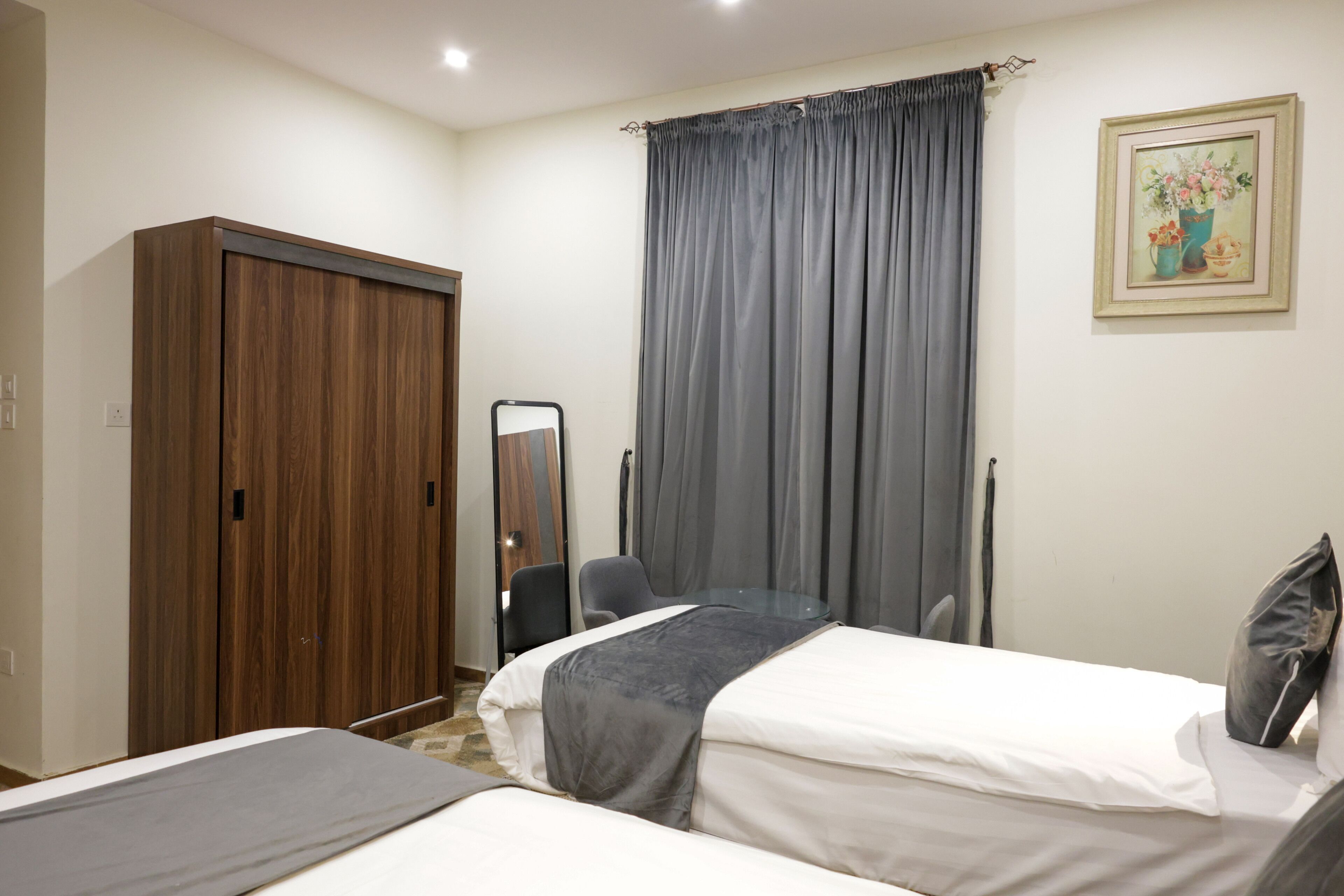 Une chambre avec deux lits, une armoire, une chaise, un miroir et un tableau accroché au mur.