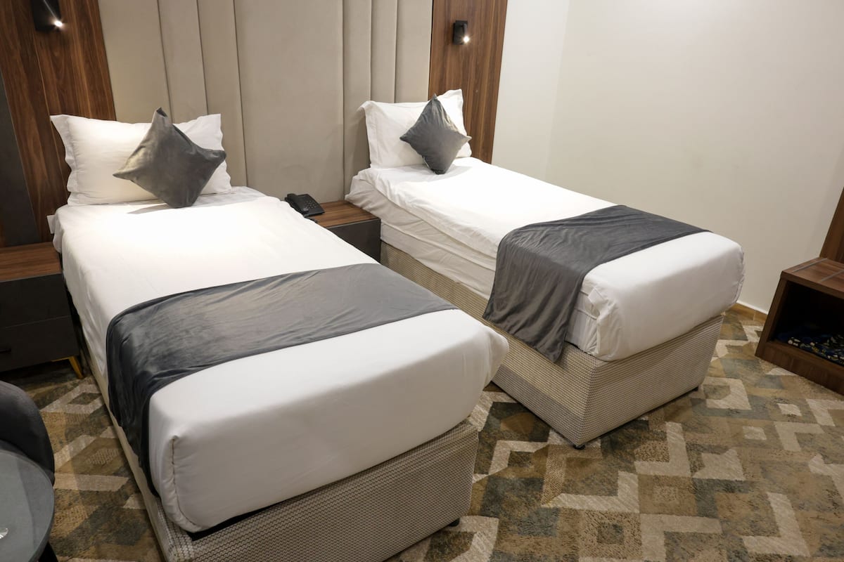 Dos camas individuales con cabeceras, una mesita de noche con un teléfono y una alfombra estampada.