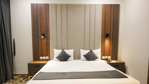 A hotel room with a large bed, two bedside tables, a wooden headboard, and a patterned floor. - Durrat Al Aziziyah Serviced Apartments (Madinah)