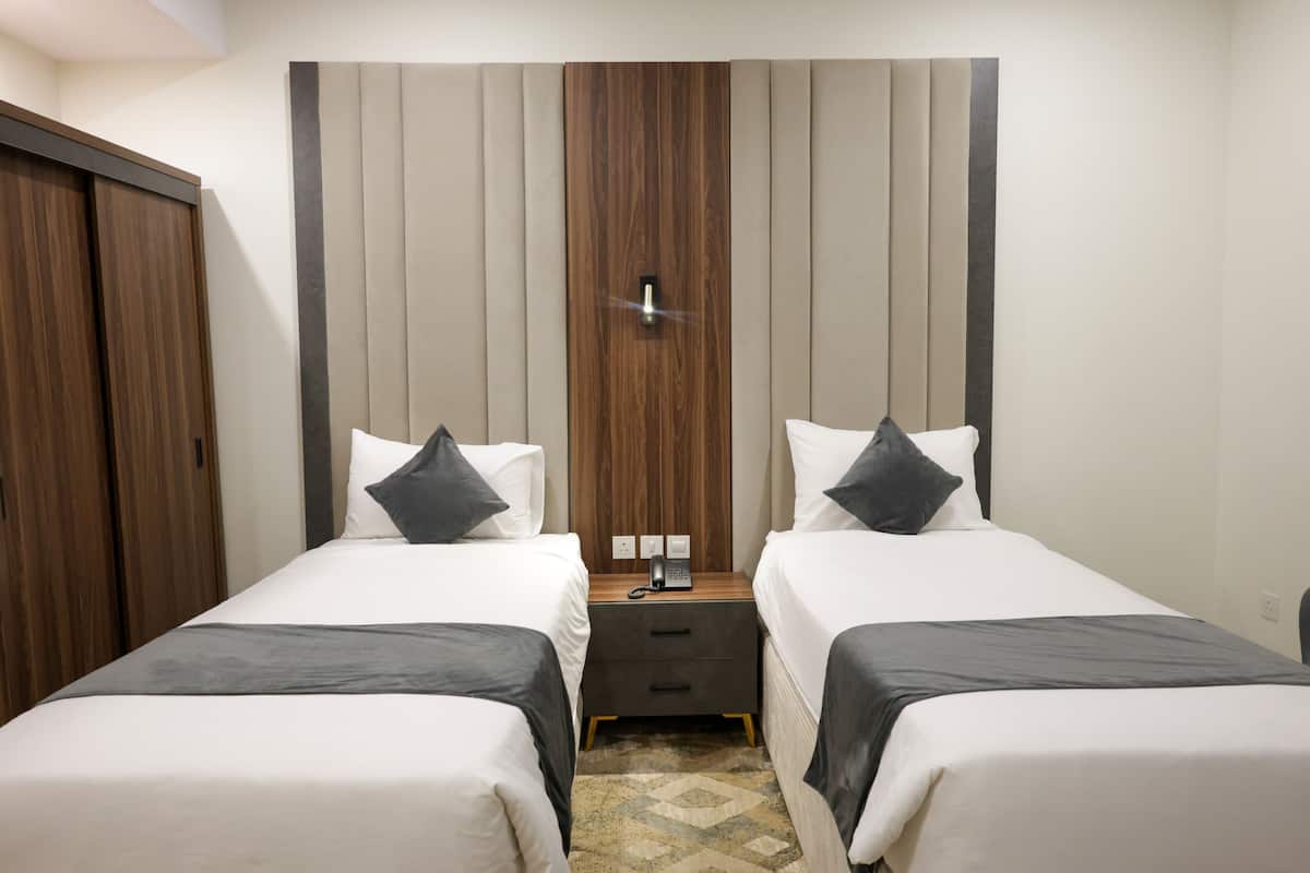 Habitación de hotel con dos camas, un armario de madera, una mesita de noche con teléfono y una lámpara fijada a la pared.