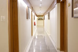 Un couloir d’hôtel avec des portes en bois, un extincteur et un tableau encadré accroché au mur.