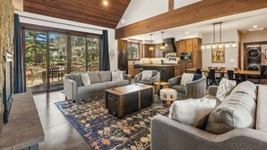 A spacious living area with a large sofa, a coffee table, and a rug. There is a kitchen in the background with wooden cabinets and a dining area. - Lucky Star Lodge | Pool & Hot Tub | Fire Pit (Durango)
