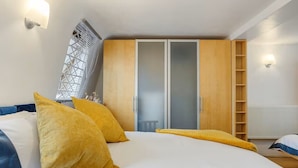 A bedroom with a bed, yellow pillows, a wardrobe, and a radiator. - Charming Mews House Near King's Cross (London)