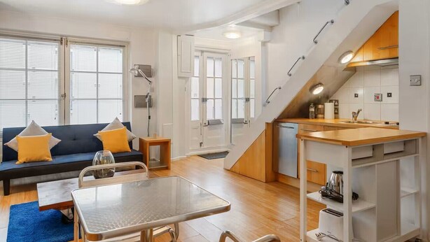 A compact living space with a sofa, dining table, kitchenette, and a staircase. - Charming Mews House Near King's Cross (London)