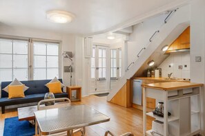 Ett kompakt bostadsutrymme med en soffa, ett matbord, ett litet kök och en trappa.