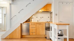 A compact kitchen with a wooden countertop, stainless steel appliances, and a white backsplash. - Charming Mews House Near King's Cross (London)