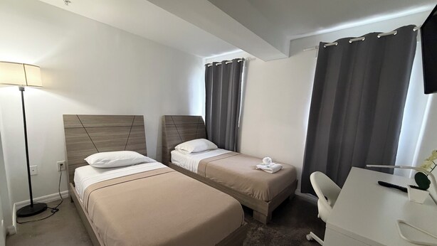 A hotel room with two beds, a desk, a chair, and a lamp. - Triangle Suites LLC (Hialeah)