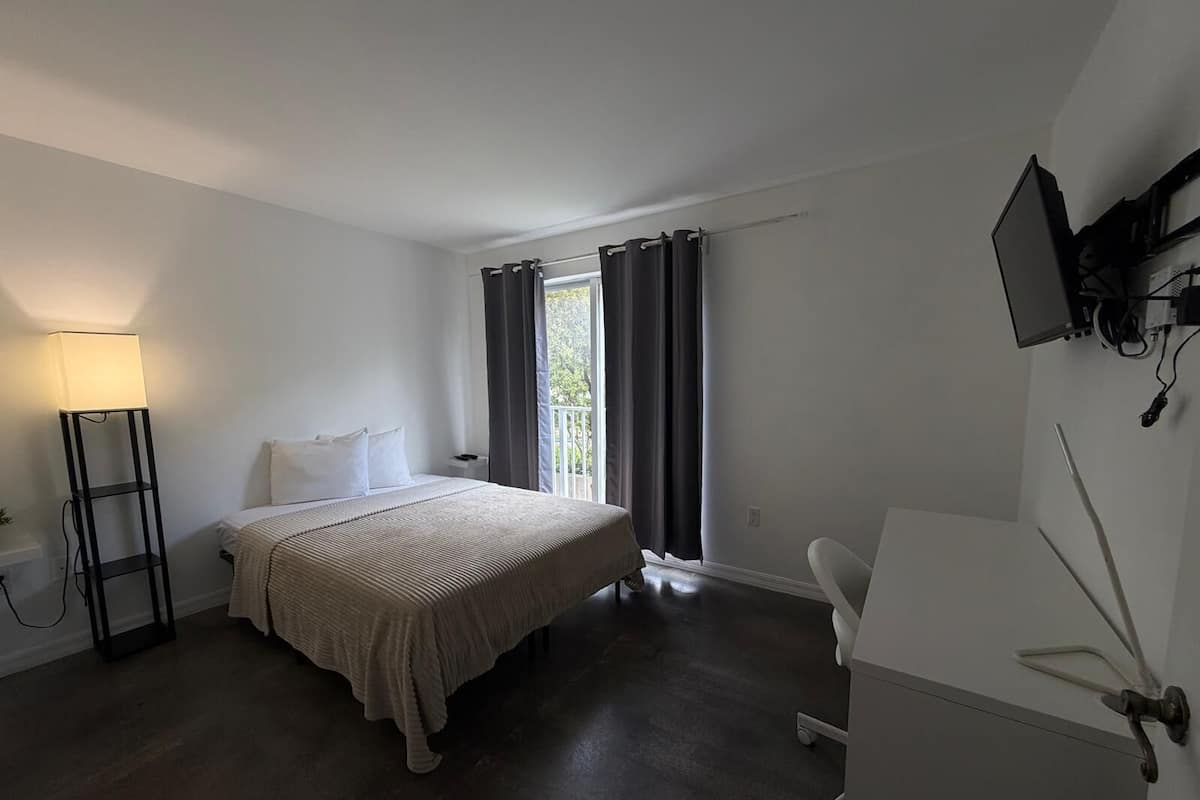 A hotel room with a bed, a desk, a chair, a TV, and a window with curtains.