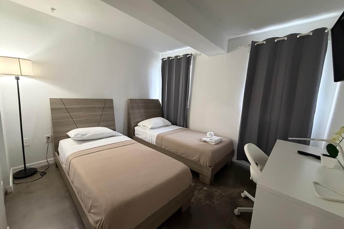 A hotel room with two beds, a desk, a chair, a lamp, and a TV.