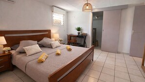 A bedroom with a wooden bed, bedside tables, a desk, a hanging light fixture, and a view of the hallway.