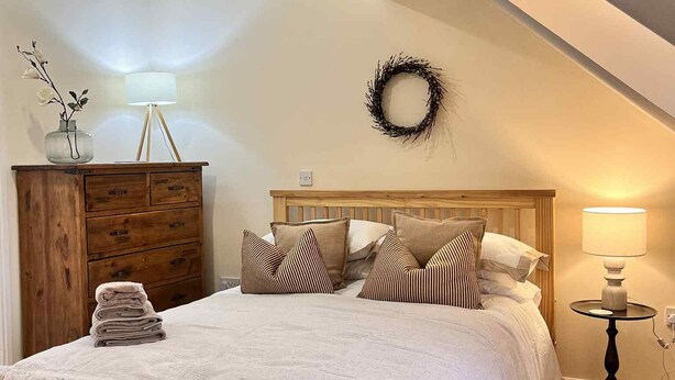Ein Schlafzimmer mit einem hölzernen Bett, einem Schminktisch, einer Lampe und einem an der Wand befestigten Kranz.