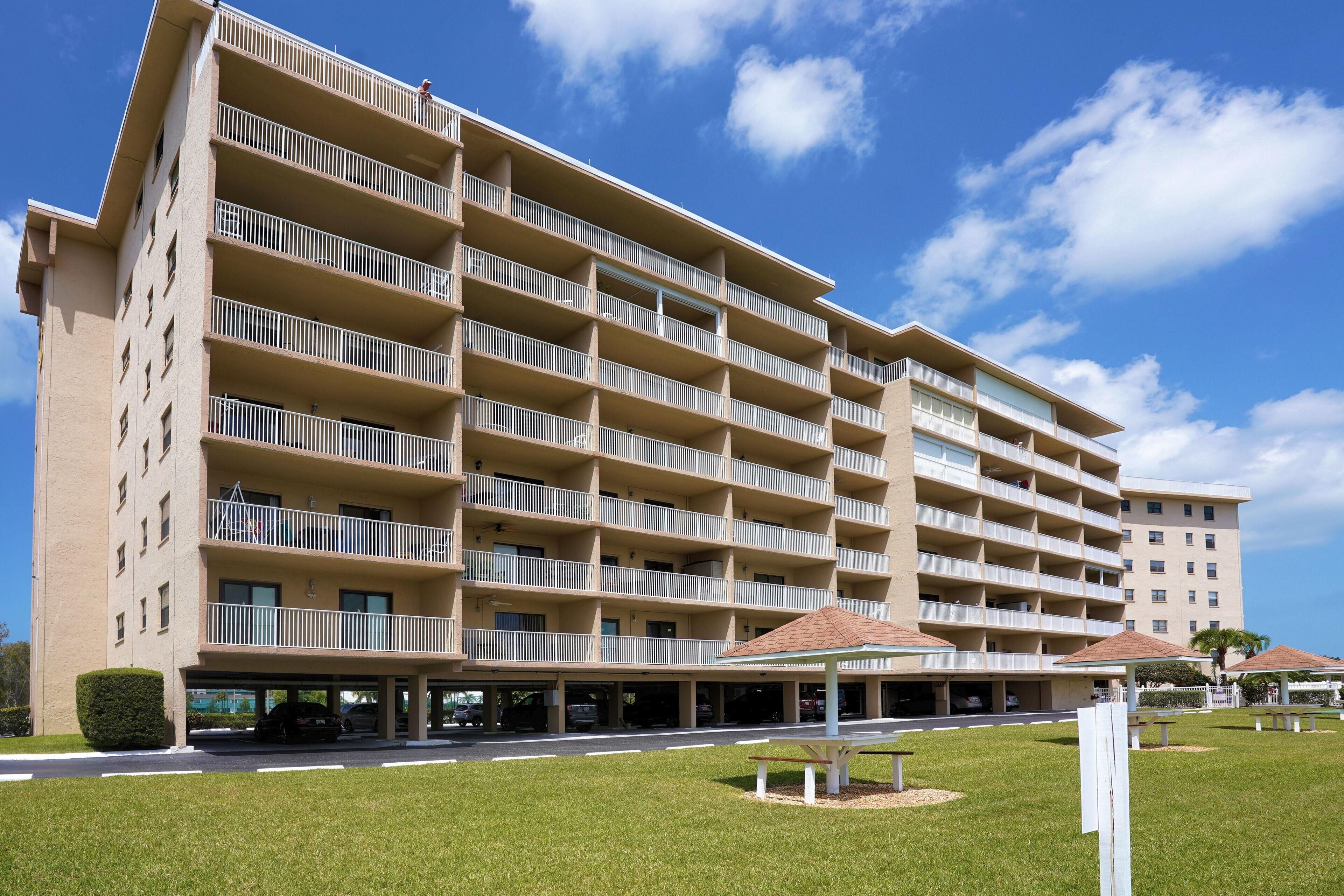 Un hotel de varios pisos con fachada plana, balcones y una zona de estacionamiento.