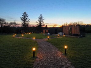 Un chemin mène à un bâtiment moderne doté de nombreuses pièces, entouré d’une zone herbeuse et d’arbres.