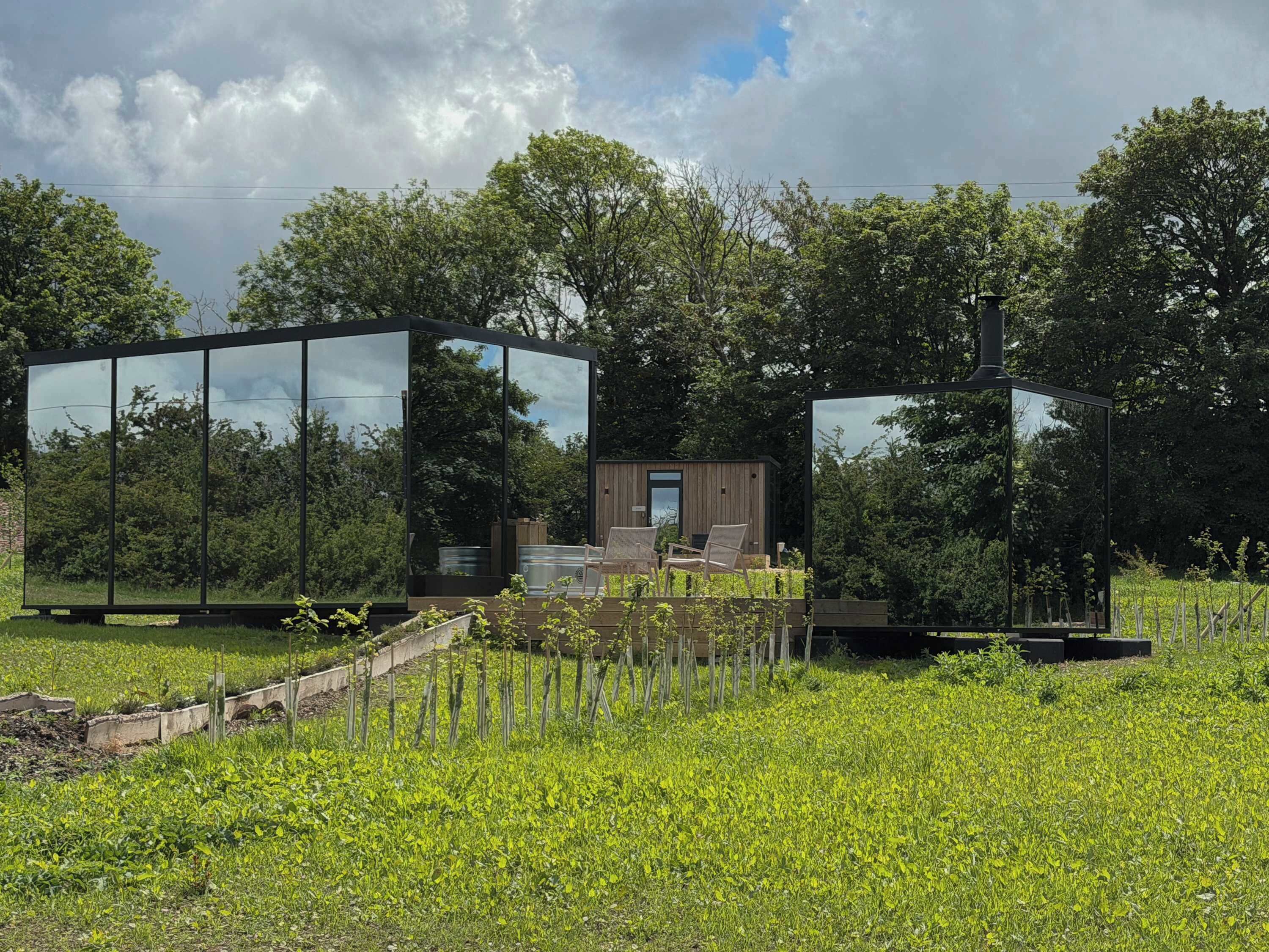 A modern outdoor structure with glass walls, a wooden deck, and a seating area.