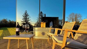 Una terraza de madera con una mesa, dos sillas, un ventanal grande y un jacuzzi.