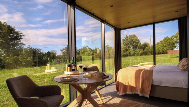 Un dormitorio moderno con un ventanal grande, una cama, una mesa de comedor y una silla.