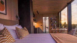 Un dormitorio moderno con una cama grande, una pequeña zona de comedor y vistas a la puesta de sol.