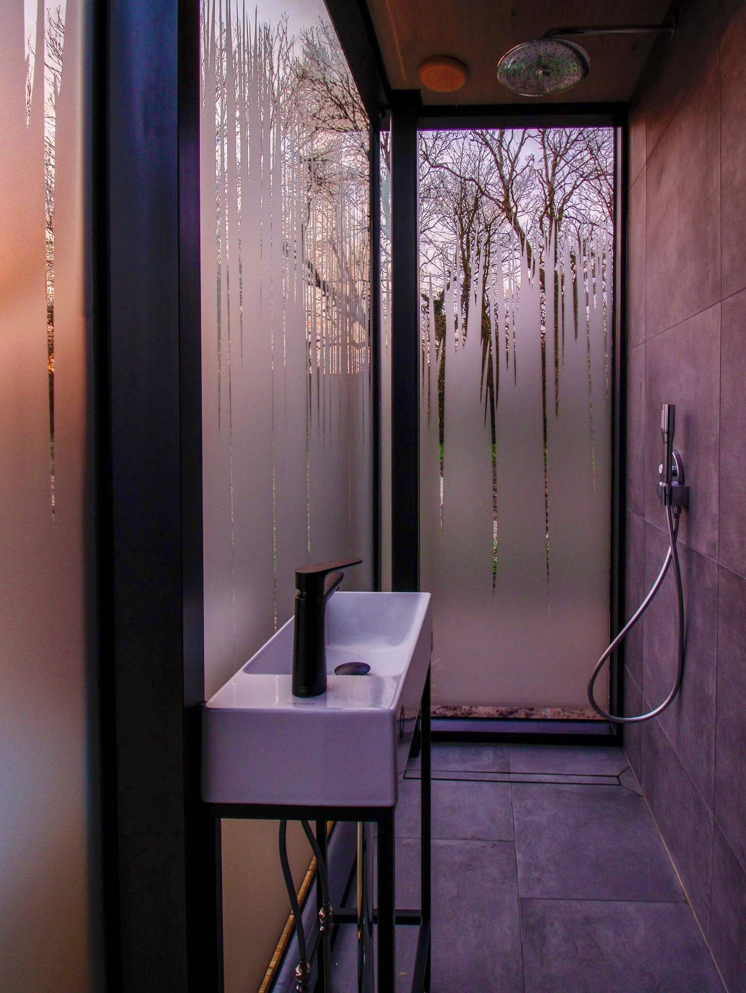Un bagno moderno con una porta in vetro satinato, un lavandino bianco e zona doccia.