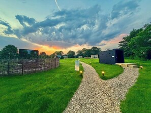 A gravel path leading to a building with a modern design, surrounded by greenery and a cloudy sky. - Mirror Cabin · Private Sauna & Plunge · Anglesey (Anglesey)