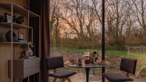 Zona pranzo moderna con un tavolo rotondo, due sedie e vista su alberi attraverso ampie finestre.