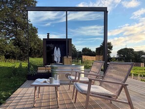 Una terraza al aire libre con sillones de descanso, una mesa con un libro y una taza, y una sauna.