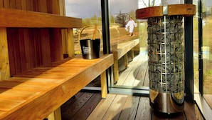 Een sauna met een houten bank, een zwarte emmer met houten handvat en een stenen heater.