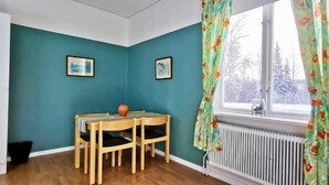 A room with teal walls, a wooden dining table with chairs, a window with curtains, and a radiator. - Kronlund Kursgård (Vindeln)