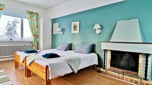 A bedroom with two single beds, a fireplace, a window with curtains, and a radiator. - Kronlund Kursgård (Vindeln)