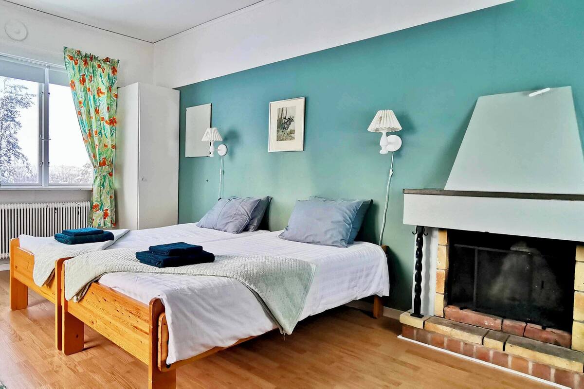 Ein Schlafzimmer mit zwei Einzelbetten, einem Kamin, einem Fenster mit Vorhängen und einer Heizung.