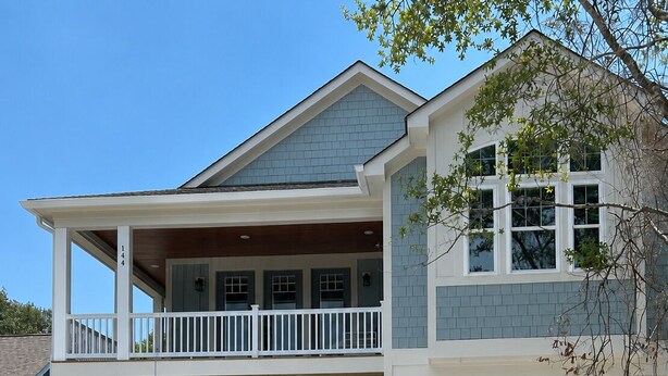 A two-story house with a covered front porch, a garage, and a staircase leading to the upper level. - Happy Tides Hideaway/NEW!/Pool/Kids Adventure Room (Oak Island)