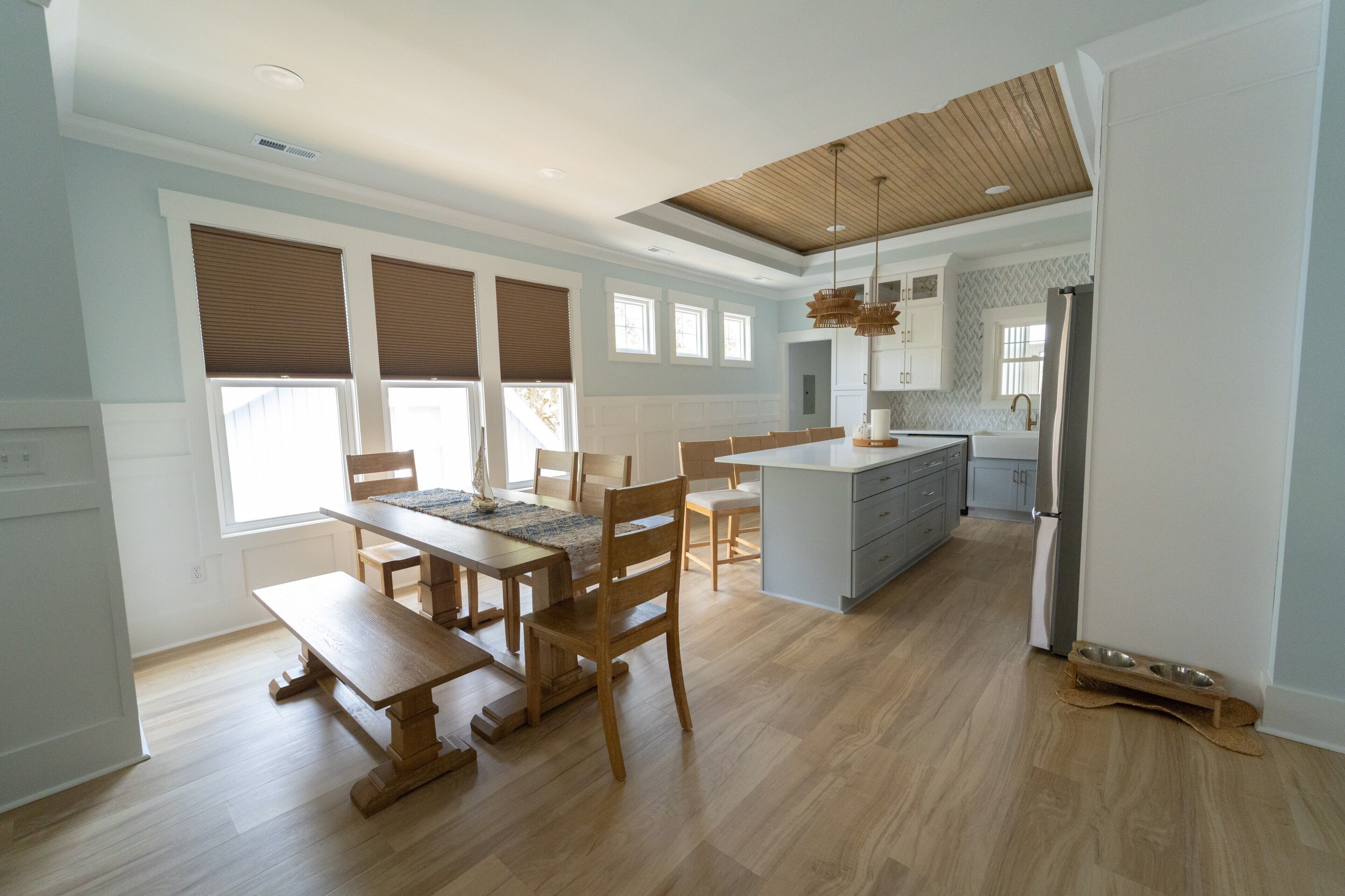 A spacious kitchen with wooden flooring, a dining area with a wooden table and benches, and a modern island with a sink.