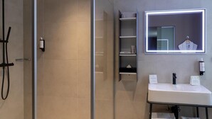 A modern bathroom with a glass shower enclosure, a white sink with a mirror above it, and a towel rack. - Hotel Restaurant l'Orchidée (Ensisheim)
