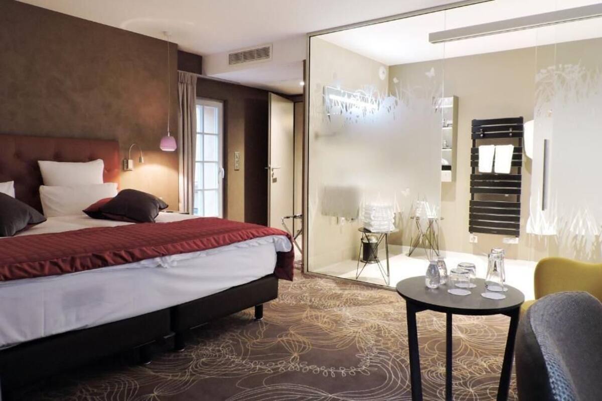 Une chambre d’hôtel avec un lit, une petite table, une chaise et un mur en verre.
