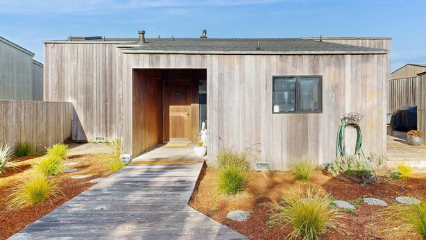Una casa moderna con fachada de madera, una puerta principal y un camino que lleva a la entrada.