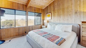 Un dormitorio con paneles de madera, una cama grande, una mesita de noche, una lámpara y una ventana con vistas.