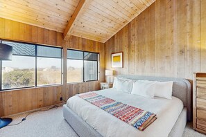 Ein Schlafzimmer mit Holzwänden, einem großen Bett, einem Nachttisch, einer Lampe und einem Fenster mit Blick.