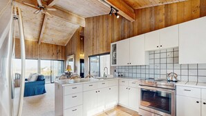 Una cocina moderna con armarios blancos, horno de acero inoxidable y techo de madera.