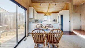 Cocina moderna con vigas de techo de madera, una isla central con asientos y un amplio ventanal corredero a una terraza exterior.
