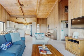 A modern interior with a wooden ceiling, a sofa, a coffee table, a television, and a kitchen area.