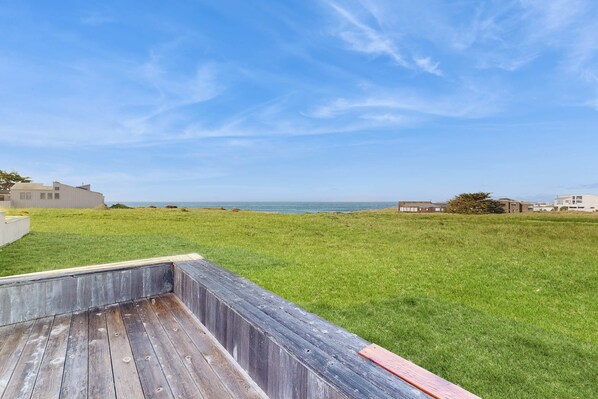 A grassy outdoor area with a wooden deck and a view of the ocean.