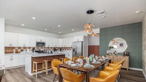 Uma cozinha moderna com armários brancos, uma ilha central e um espaço de jantar com cadeiras amarelas e uma mesa de madeira.