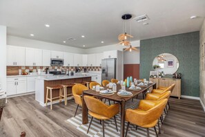 Une cuisine moderne avec des meubles blancs, un îlot central et un coin repas agrémenté de chaises jaunes et d’une table en bois.