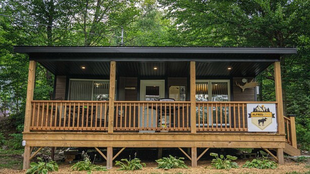 A wooden cabin with a porch, a sign with a moose, and a door. - Nature & Wildlife Escape | Alfred Shack (Frampton)