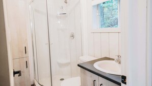 A bathroom with a glass shower enclosure, a white toilet, a sink with a black countertop, and wooden cabinets. - Nature & Wildlife Escape | Alfred Shack (Frampton)