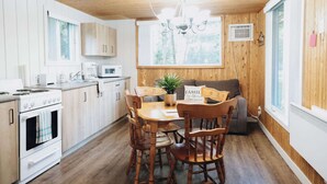 A wooden-paneled kitchen with a dining table, chairs, a stove, and a microwave. - Nature & Wildlife Escape | Alfred Shack (Frampton)