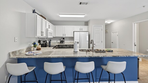 Une cuisine moderne avec des meubles blancs, un mur d’accent bleu et un îlot en marbre agrémenté de tabourets de bar.